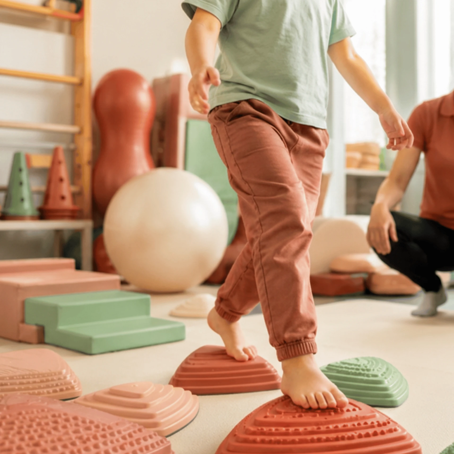 Kind loopt op oefenstapstenen tijdens een pediatrische kinesitherapiesessie.